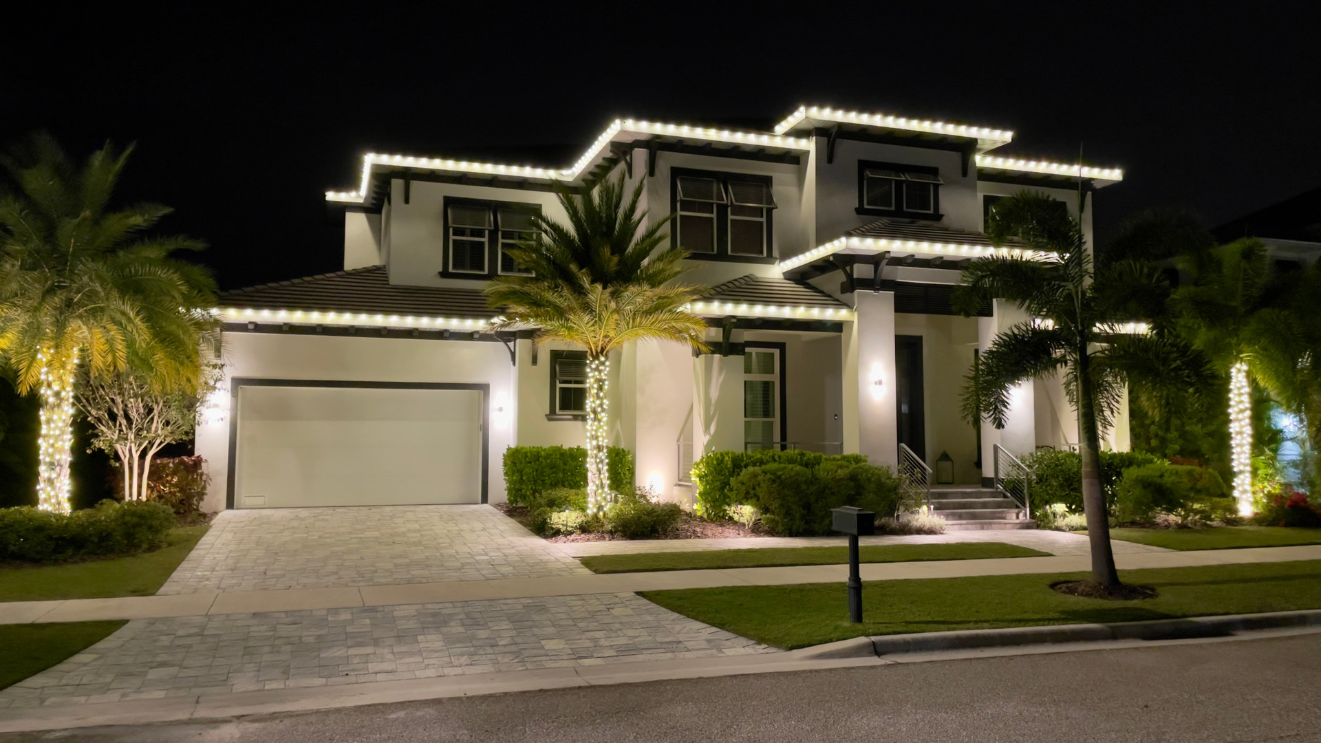 The same home with warm-white Christmas roofline and palm lights on.