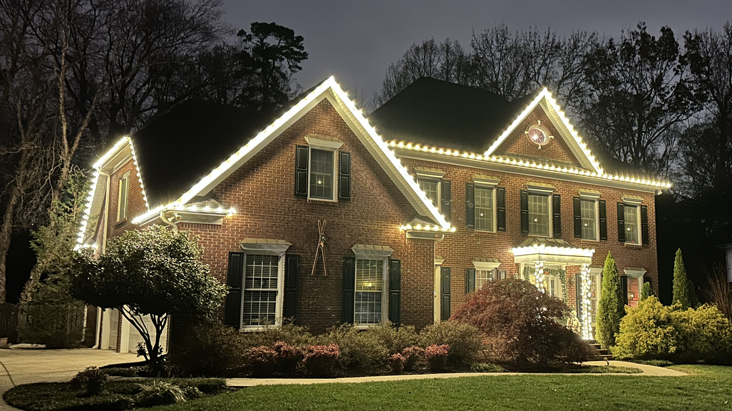 Warm-white roofline and porch-column lights on a large brick home.
