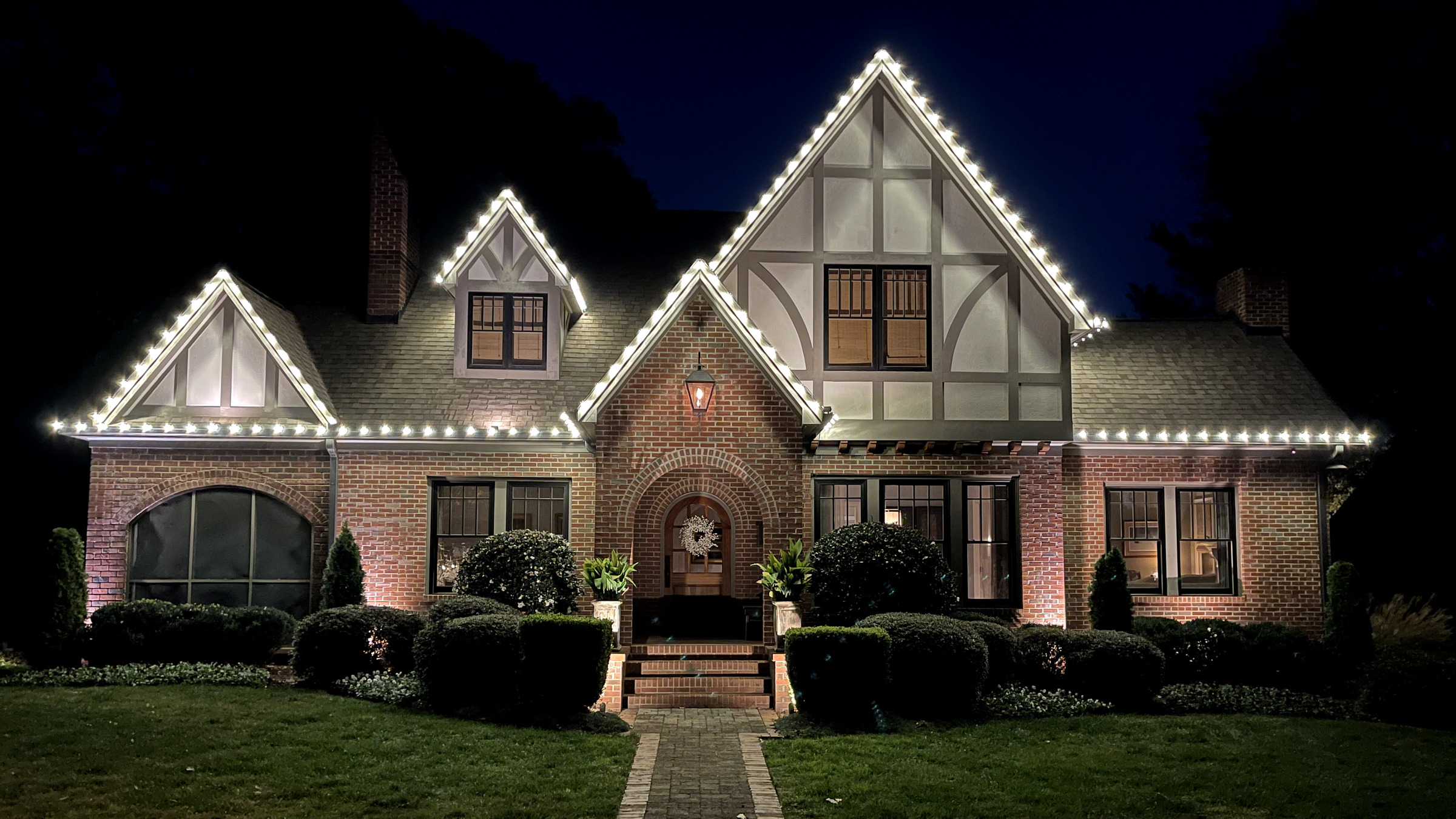 Warm-white Christmas lights tracing Tudor gables and a roofline.