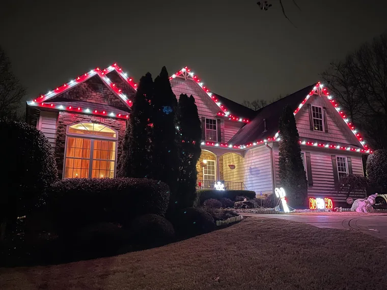 Red-and-white Christmas lights outlining the gables and entrance of a stone and siding home.